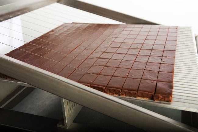 Handwerkliches Schneiden der Pralinenfüllung mit einer Harfe.