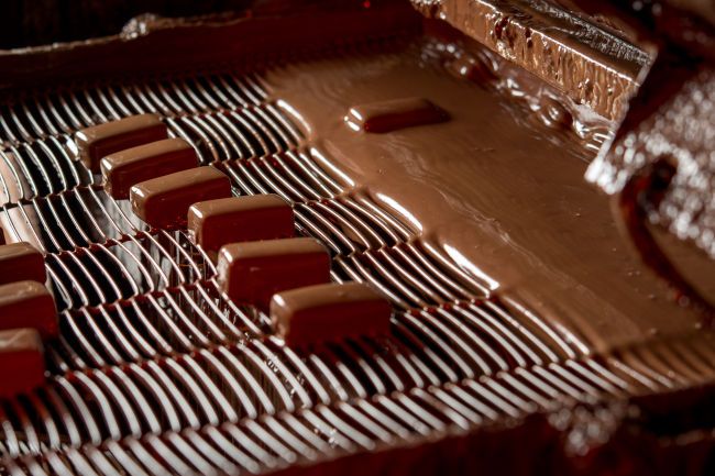 Frisch überzogene Pralinen auf einer kleinen Überziehanlage.