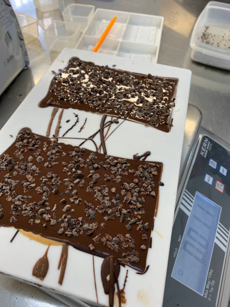 Die frisch gegossenen Tafelschokoladen werden von Hand mit Kakaonibs bestreut. Die frisch gegossenen Tafelschokoladen werden von Hand mit Kakaonibs bestreut.